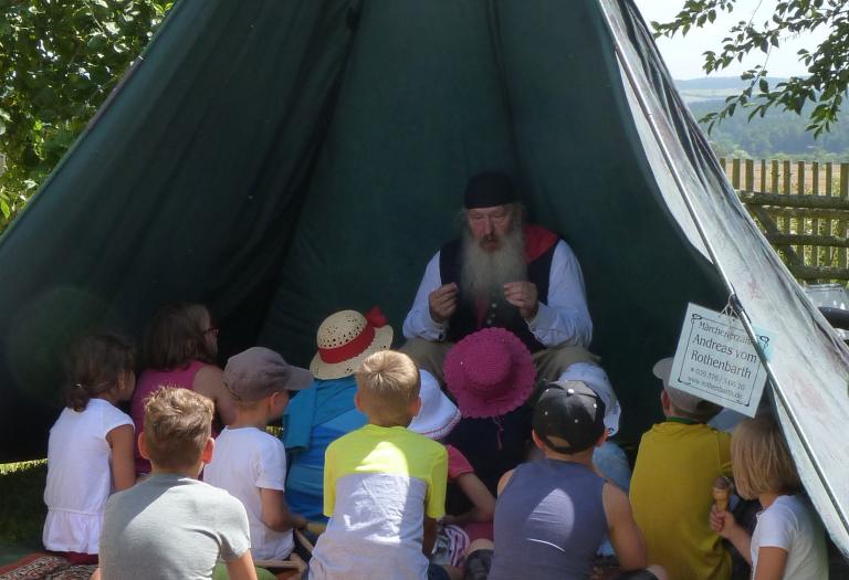 In einem offenen Zelt erklärt ein Mann Kindern etwas Spannendes.