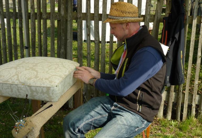 im Freien näht ein Polsterer mit der Hand an einer Sitzauflage